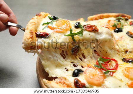 Woman taking slice of cheese pizza with seafood at table, closeup