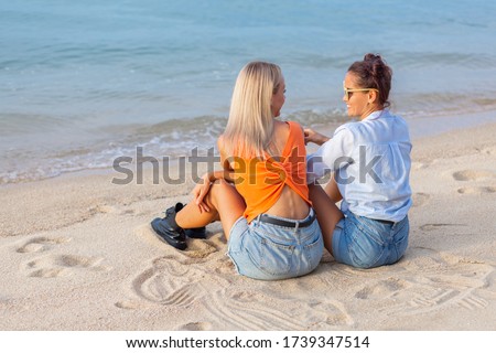 summer vacation, holidays, travel and people concept - two young women in heart sunglasses and casual clothes on beach. Friends having fun on beach near water.