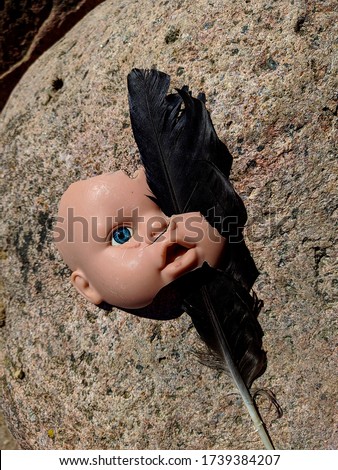 scary and broken doll face with one blue eye along with a black feather of a raven