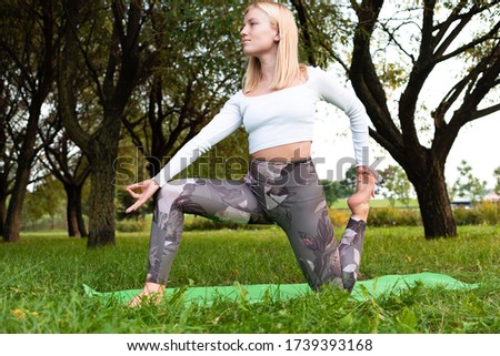 Blonde in a white t-shirt and sports leggings doing yoga on a rug in the park