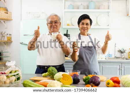 Portrait of an elderly Asian couple cooking in the home kitchen. They have a smiling face, happy, and show their milk in their hands. Retirees drink milk to make bones strong. Prevent osteoporosis. Royalty-Free Stock Photo #1739406662