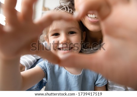 Close up little girl wearing princess diadem and mother showing heart sign with hands, looking through fingers at camera, taking selfie, happy mum and smiling daughter having fun together Royalty-Free Stock Photo #1739417519