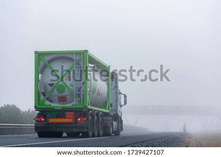 Truck transporting container with dangerous goods circulating on a highway with dense fog