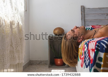 Young man with medium long blonde hair stretched out on the bed looking up. Loneliness and home life concept.