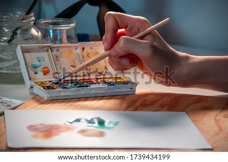 photograph of a girl painting abstract forms with watercolors and a brush, on a wooden board and with warm light