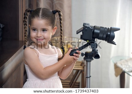 portrait of a little girl with pigtails, who holds with both hands a tripod with a camera