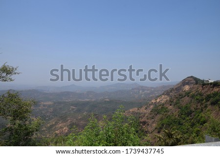 Stock photo of beautiful mountain range under blue sky cover with green trees , pants and grass. Farmhouse on the top of mountain edge ,Picture captured during summer season at Kolhapur, India.