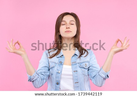 Pretty smiling girl dressed in white t-shirt, denim jacket on pink background. Young woman is relaxing, meditating, practicing yoga, keeping calm. Female gesturing. Emotional portrait concept.