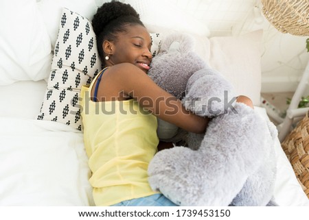 beautiful young african woman lies on bed with soft toy