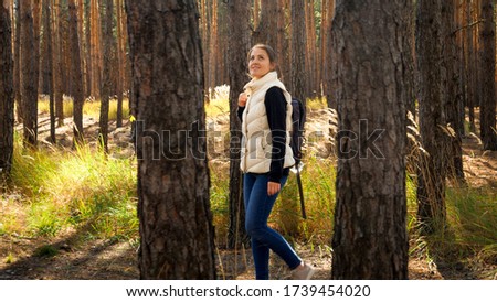 Beautiful young female tourist looking on high pine trees while walking in autumn forest.