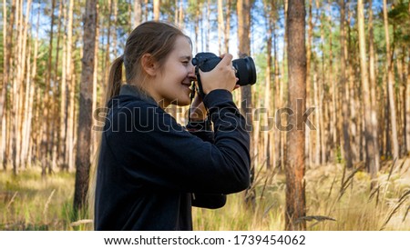 Portrait of smiling wild nature female photographer making photograph on digital camera at forest.