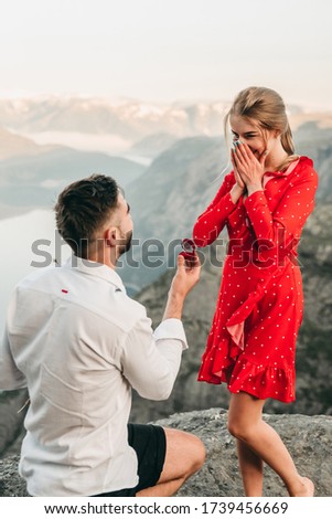 A man stands on his knee near the cliff and makes a creative proposal to a woman traveling in trolltunga, Norway. Emotional couple in love, engagement, rocks, nature, fjords. She said yes on the top. Royalty-Free Stock Photo #1739456669