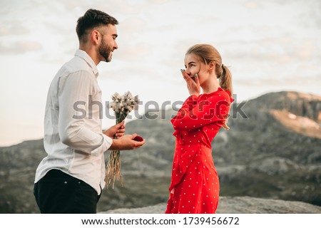A man stands on his knee near the cliff and makes a creative proposal to a woman traveling in trolltunga, Norway. Emotional couple in love, engagement, rocks, nature, fjords. She said yes on the top. Royalty-Free Stock Photo #1739456672