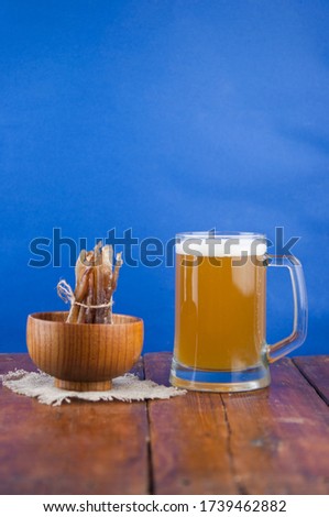 Dried fish in the shape of a straw with beer glass on wooden table. Salted fish delicacies on a table. 