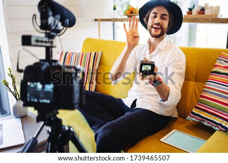 Happy blogger hosting and recording his video show and streaming it to the internet and world network, sitting at home on his sofa and using action camera