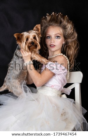 close up studio portrait of beautiful little cheerful blonde girl in
ball gown.  Child makeup. Princess with dog