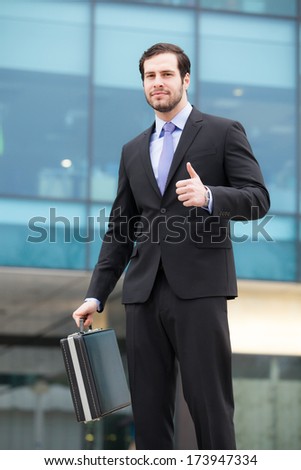 businessman showing ok sign in front of an office building
