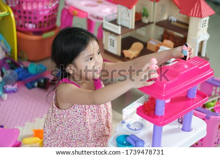 Asian child cute or kid girl smile and thinking play kitchen toy for learning education and build house or family home with finance investment or future development with real estate at nursery school