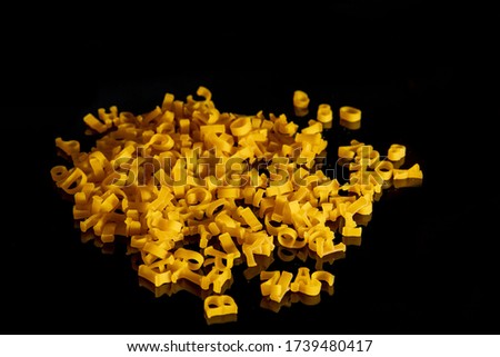 Close up of raw pasta alphabet scattered on a black background. Kids food.