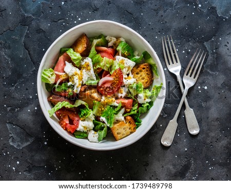 Salad with fresh tomatoes, crunchy ciabatta bread, mozzarella cheese, green salad with olive oil, french mustard, lemon dressing on a dark background, top view Royalty-Free Stock Photo #1739489798
