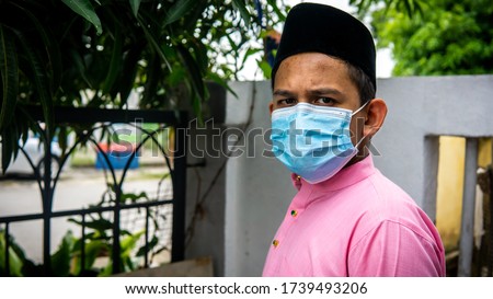 A portrait of young Asian Malay man with Baju Melayu cloth and Songkok wearing a 3 layer face mask during the Eid al-Fitr celebration in Coronavirus season. Hygiene lifestyle. New normal concept.