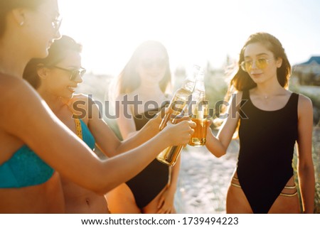 Nice girls cheers and drink beers on the beach at sunset. Young four girl in bikini enjoying on beach holiday.  Summer holidays, vacation, relax and lifestyle concept.