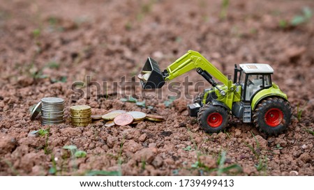 Closeup Of Small green Agricultural Toy Tractor loading money coins, Icon Farmer Machinery, Agriculture Business Concept