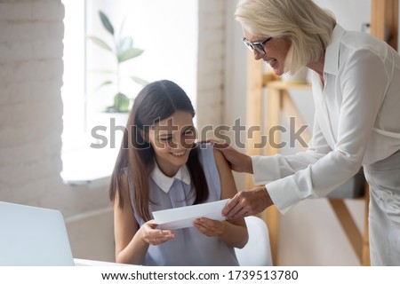 Excited millennial female employee receive money compensation reward for good job results from businesswoman, happy young woman worker get monetary gratitude for successful work from boss