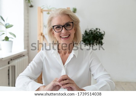 Headshot close up view of smiling middle-aged businesswoman in glasses have video call with business client, happy mature female employee speak talk on WebCam, engaged in web conference in office