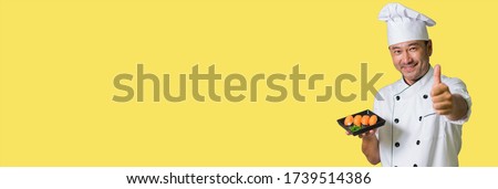 Asian chef showing plate with sushi and OK. Focus on sushi. Banner edition. Isolated on yellow background.