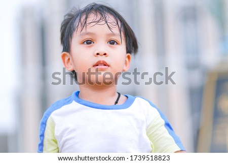 Close up image of cute little kid looking straight and playing in a park with sweat on his face, head shot portrait of small child walking with absent minded face, candid image of small boy Royalty-Free Stock Photo #1739518823