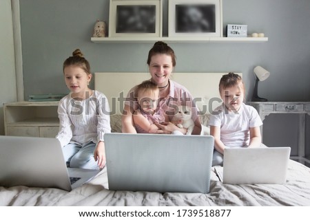 Caucasian Mom and Three sibling children are sitting on bed with laptops, mother with many children works remotely. concept digital addiction, home, distance learning online, remote work motherhood