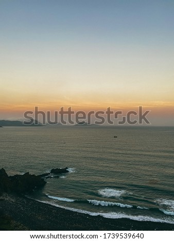 Sunset on the sea with a panoramic view from the top of the cliff. View of the rocky sea shore, waves on the shore. Mountains on the horizon. Beautiful sky color from the setting sun