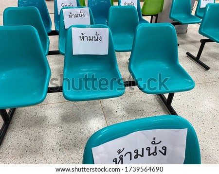 A row of plastic chairs in public place with a sign “do not sit” in Thai. It’s followed COVID19 campaign, social distancing campaign. To stop spreading germs and viruses.