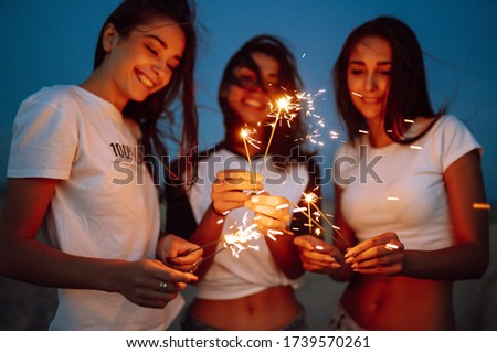 The sparklers in the hands of young girls on the beach. Three girls enjoying party on beach with sparklers. Summer holidays, vacation, relax and lifestyle concept.