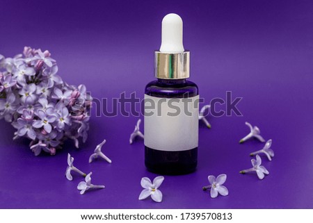 Composition with lilac flowers and a cosmetic bottle of essential oil on a lilac background, top view, place to record