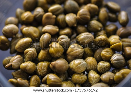 pickled capers in a glass bowl on a dark background, top view close up