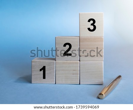 wooden cube blocks stairs steps with number 1, 2, 3 arranged on stacks and pen isolated on blue background. Business growth concept Royalty-Free Stock Photo #1739594069