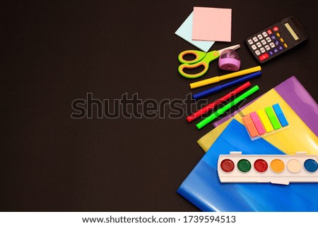 School accessories (pencils, pens, calculator, paper clips, paper, felt-tip pens, paints, scissors, textbook covers) on black paper background. School preparation concept