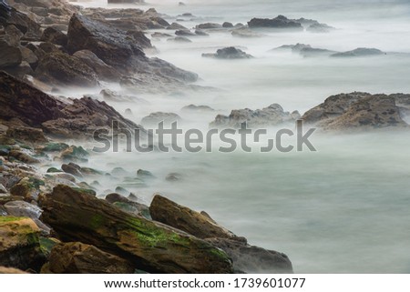 Long exposure photography of sea waves breaking against the rocks of the breakwater in Porto Novo, Portugal.