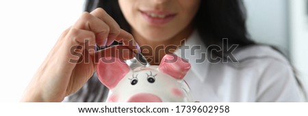Nice girl puts a coin in ceramic pig figurine. Know assortment stores and, reaching out only hand, immediately get into right thing. Saving time and money when using business shopping