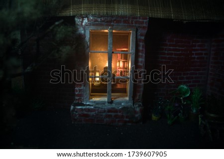 A realistic dollhouse living room with furniture and window at night. Man sitting on table in dark room. Concept of stay home during global virus pandemic. Selective focus.
