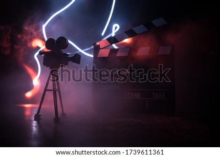 Movie concept. Miniature movie set on dark toned background with fog and empty space. Silhouette of vintage camera on tripod and clapboard. Selective focus