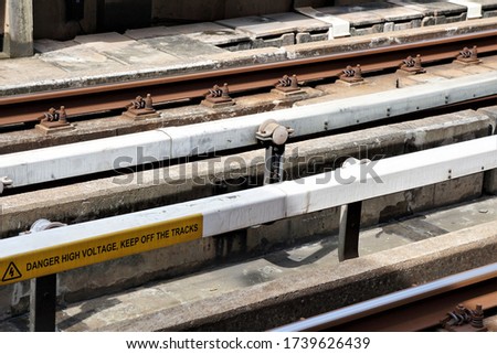 Electric train tracks that has letter notification about danger high voltage, keep off the tracks. 
