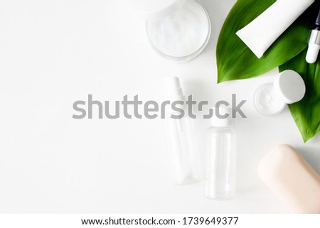 White squeeze tube, bottles of cream, dropper glass serum, soap, continers with green tropical leaves flat lay on white background top view copy space. Beauty skincare, natural cosmetic. Stock photo.