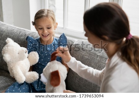 Overjoyed little girl sit on sofa have fun playing toys with caring young mother or nanny, playful mom engaged in funny game with small preschooler daughter, enjoy family weekend entertainment