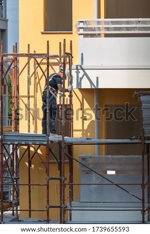 Worker with Blue Hardhat at Work on a Scaffold in a Building Site for the Construction of a Building.