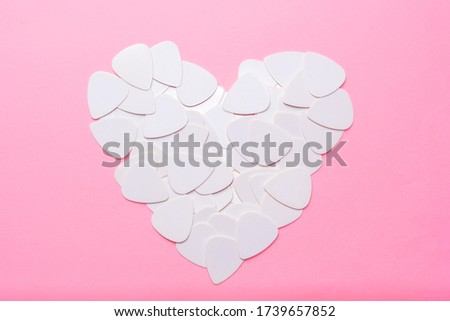 Light pink background with a bunch of white guitar picks folded in the shape of a heart.