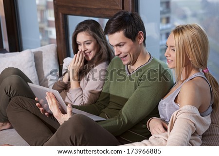 Friends sitting together on the sofa and watching movie on on laptop pc and chatting 