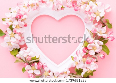 Frame of white heart shape and apple blossoms on light pink table background. Pastel color. Love and happiness concept. Empty place for cute, emotional, sentimental text, quote or sayings. Closeup.